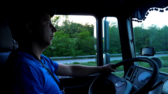 日落时分，卡车司机在乡间行驶的侧面图。戴着帽子的人控制着他的卡车，注意观察着道路。货车车厢内的景象。货物运输的概念。慢镜头视频下载