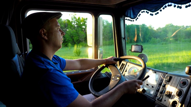 傍晚，一辆卡车在乡间行驶。戴着帽子的男人控制着他的卡车，享受着旅程。查看车厢内。运输的物流概念。慢镜头视频下载