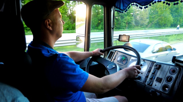 卡车司机骑在乡村的特写。戴着帽子的人控制着他的卡车，小心地看着交通。明亮的夕阳映照在汽车的侧镜上。慢镜头:卡车司机在乡间行驶的特写。戴着帽子的人视频下载