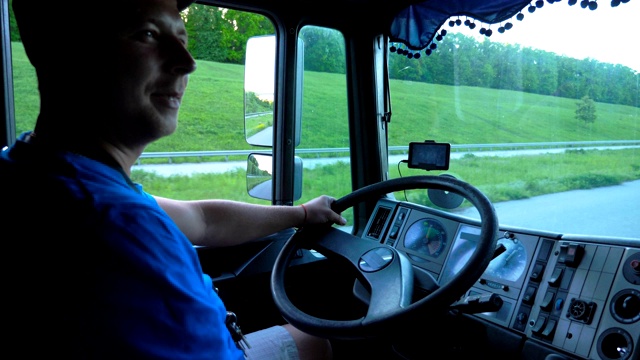 在夕阳的背景下，微笑的卡车司机穿过乡村的侧面。快乐的人控制着他的卡车，享受着旅程。货车车厢内的景象。内景慢动作特写视频下载
