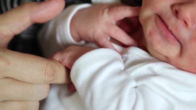 可爱的新生婴儿手牵着爸爸的手指。父亲抚养新生儿视频素材
