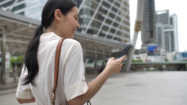 一名亚洲女性在城市中行走并使用智能手机视频下载
