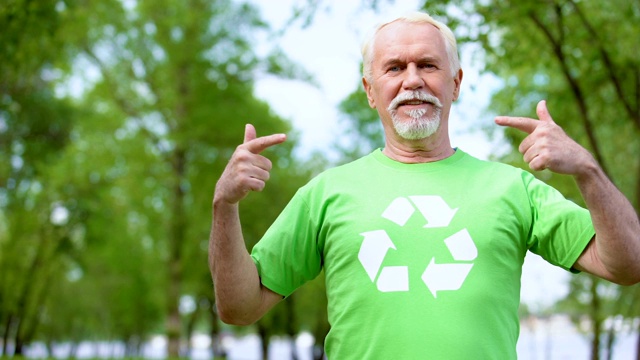 微笑的成熟男性指着绿色t恤上的回收标志，生态视频下载