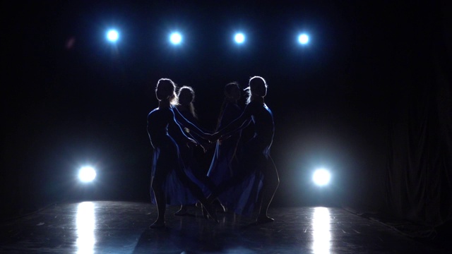 四个芭蕾舞演员在聚光灯下的黑暗中跳现代芭蕾舞。慢动作视频下载