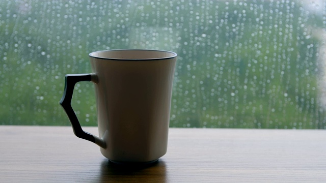咖啡杯放在木桌上，背景是雨滴视频素材