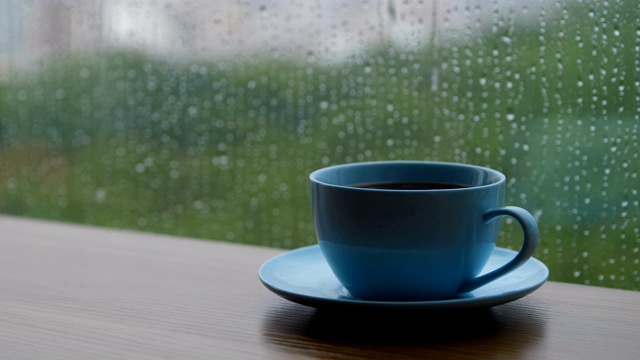 咖啡杯放在木桌上，背景是雨滴视频素材