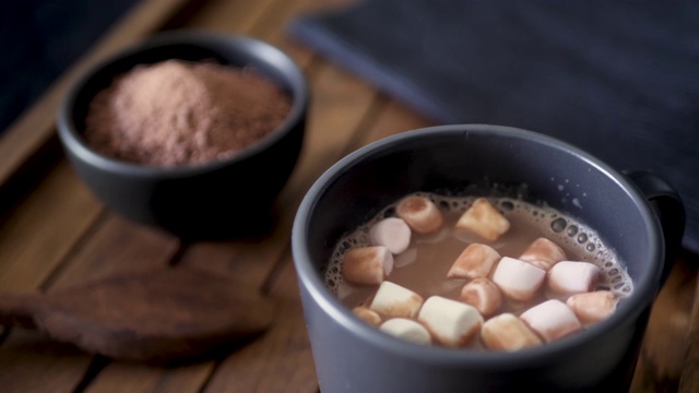 将迷你棉花糖放入一杯热巧克力中。深色木背景。慢镜头50%。视频素材