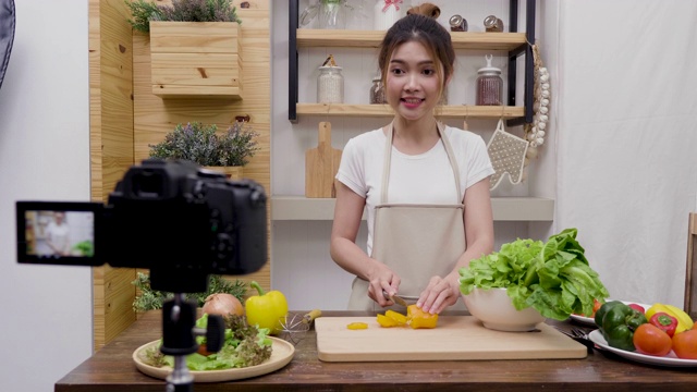 年轻的亚洲女性美食博主说话，同时录制视频准备绿色沙拉在厨房，教程视频到社交网络通过互联网在家概念视频素材