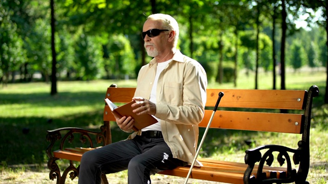 心烦意乱的盲人退休男子厌倦了盲文书，感到沮丧独自在公园视频素材