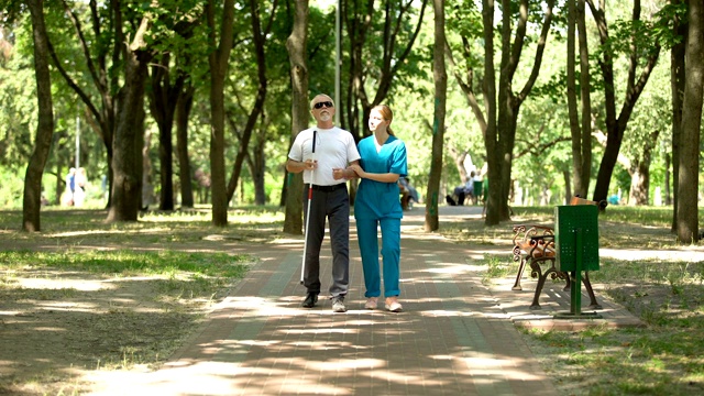 年轻护士抱着盲人老人在公园散步，视力恢复诊所视频素材