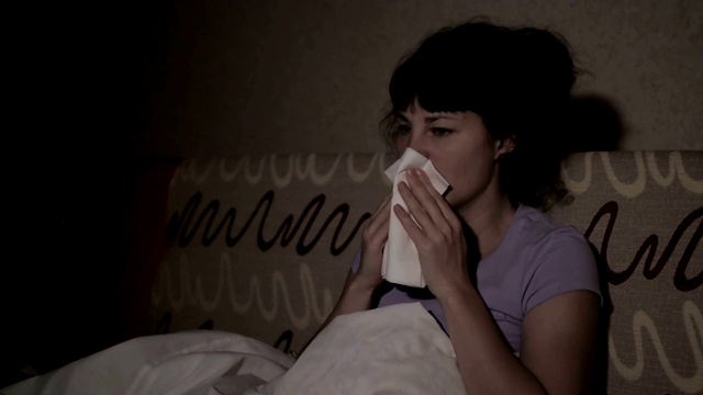 一个生病的女人晚上在家里的沙发上打喷嚏。女孩流鼻涕，拿纸巾，流感症状。医疗保健和医疗理念。感冒是流感的感染。视频素材