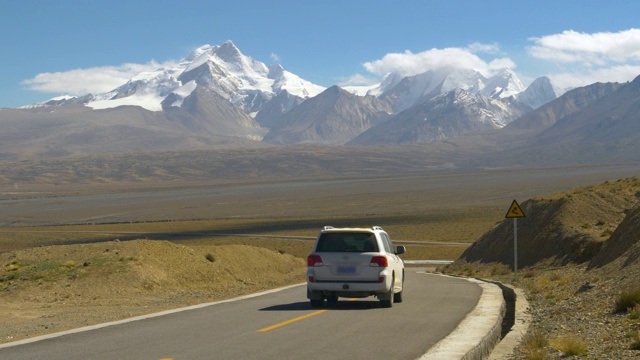 一辆白色的SUV行驶在空旷的柏油路上，通往雪山。视频素材