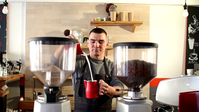 一个男人在咖啡店里当咖啡师，他把牛奶倒进一杯咖啡里。视频素材