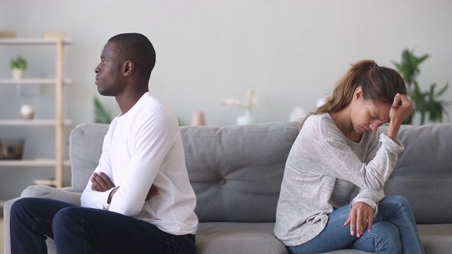 不快乐的顽固的混血年轻夫妇分别坐在沙发上视频素材