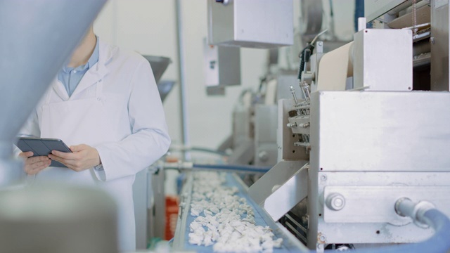 两名年轻男性质量主管或食品技术人员正在检查饺子食品厂的自动化生产。7 .员工使用平板电脑工作。他们穿着白色的工作袍。视频素材