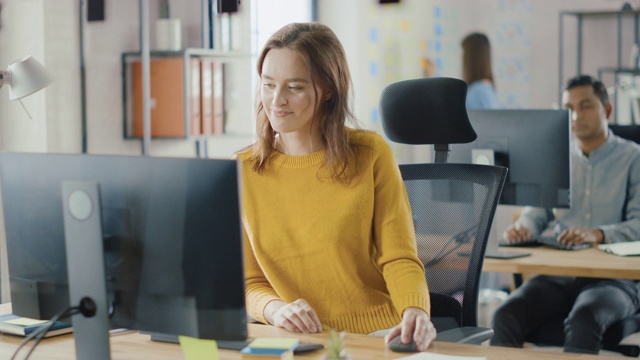 美丽而聪明的红发女专家坐在她的办公桌上工作在一台台式电脑上。明亮和现代的开放空间办公室与时尚的人体工程学家具为有才华的创造性的人视频素材
