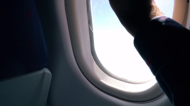 镜头靠近:男子打开飞机窗户，让眩目的光线进入机舱视频素材