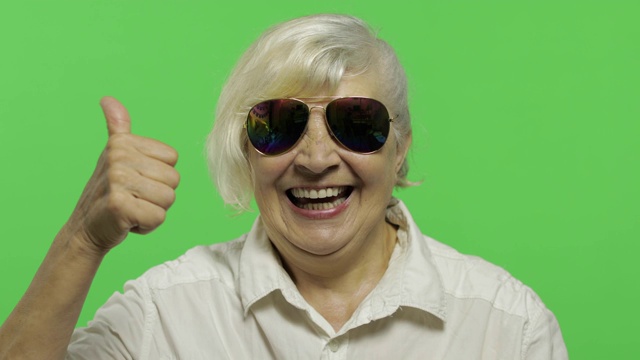 一位戴着墨镜的老妇人翘起大拇指，露出微笑。色度键视频下载