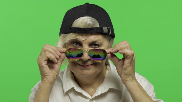 一位戴着太阳镜和帽子的老妇人微笑着。老祖母。色度键视频下载