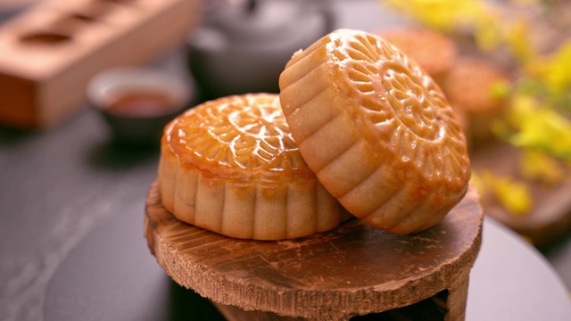 美丽的月饼在木托盘旋转，茶和花在黑石板背景。中国传统中秋节概念视频。视频素材