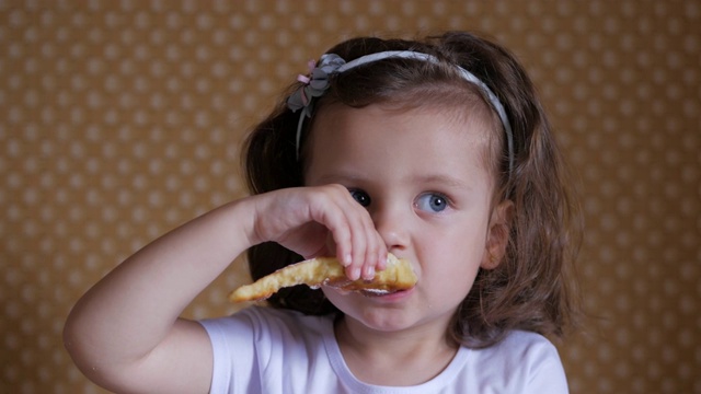快乐的小女孩穿着白色t恤坐在桌子旁吃着自制的蛋糕。甜食和儿童的概念。视频素材