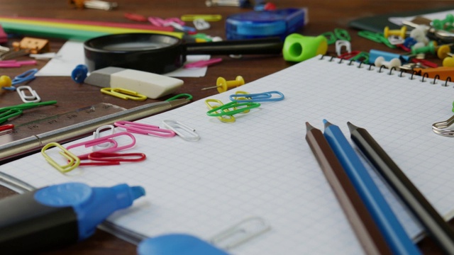 彩色铅笔，回形针和笔记本在棕色木制的书桌上视频下载