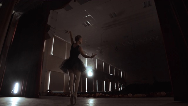 慢动作:首席芭蕾舞演员穿着黑色礼服，表演旋转和优美的舞蹈动作。摄像机在万向节上移动。视频素材