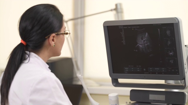 一个近距离的专业女性超声波检查看着超声波机器监视器，而执行医疗检查。医疗保健的概念视频素材