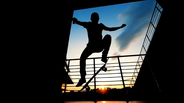 滑板运动员剪影。一个十几岁的滑冰运动员在夕阳的背景下举起他的滑板。视频素材