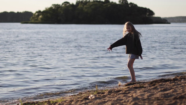 在落日的背景下，美丽的女孩赤脚走在湖边。视频素材