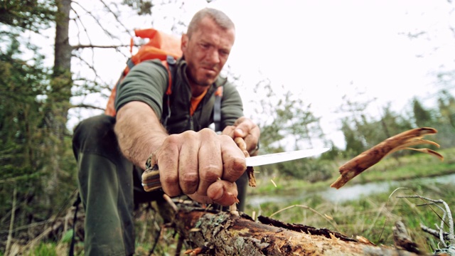男性野外生存专家用他的刀在野外磨一根棍子的末端视频素材