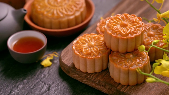 美丽的月饼在木托盘与茶和花在黑石板背景。中国传统的中秋节观念。视频素材