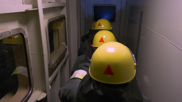 在黑暗的隧道中进行救援行动，身着防护服和黄色头盔的救援人员的背影。视频下载