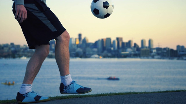 脚杂耍足球近距离与滨水城市天际线背景视频下载