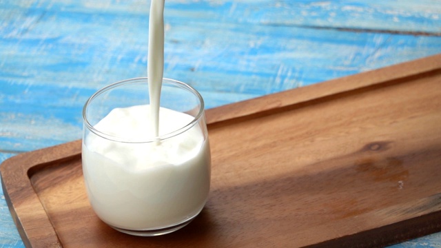 一瓶牛奶和一杯牛奶放在蓝色的木桌上，健康的乳品理念视频素材