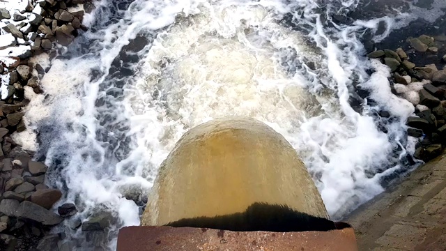 从生锈的大管道里排出的废水以一团团的蒸汽流进河里视频素材
