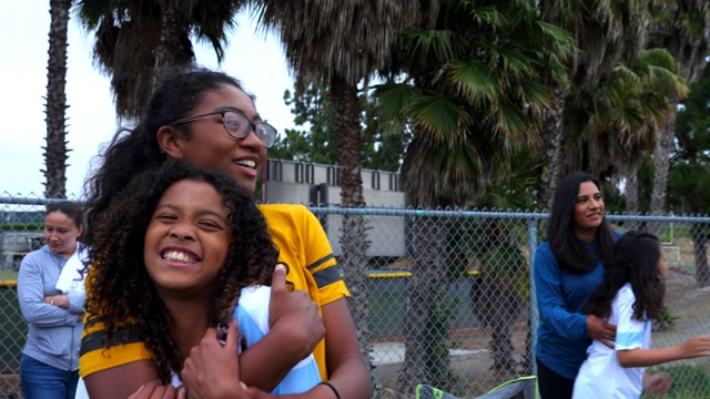 微笑的年轻女足球运动员在场边拥抱姐姐视频素材