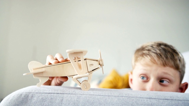 男孩玩木制飞机玩具模型。他把它“落地”在客厅的沙发扶手上。快乐童年概念慢动作视频。视频素材