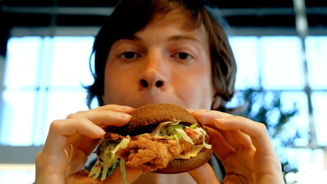 黑眼睛的家伙在模糊的窗户边吃着美味的汉堡视频素材