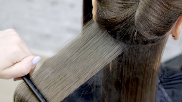 美发师在美容院为一个黑发女孩做头发分层。近距离视频下载