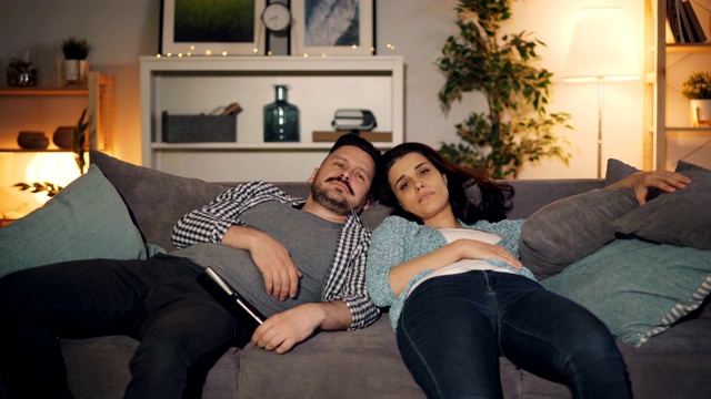 又累又困的人们男男女女在家里的沙发上看电视打哈欠视频素材