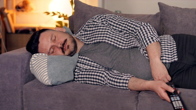 一个穿着便服的家伙拿着电视遥控器睡在家里的沙发上视频素材