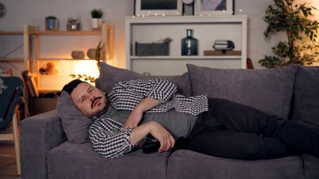 困倦的人看电视吃爆米花独自躺在家里的沙发上视频素材