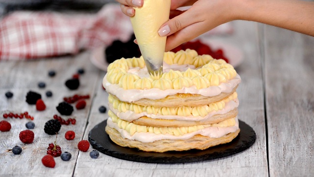 女糕点师用挤花袋和旋转蛋糕架在家庭厨房的桌子上用奶油糖霜装饰蛋糕视频下载