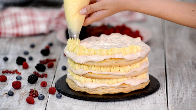 女糕点师用挤花袋和旋转蛋糕架在家庭厨房的桌子上用奶油糖霜装饰蛋糕。视频下载