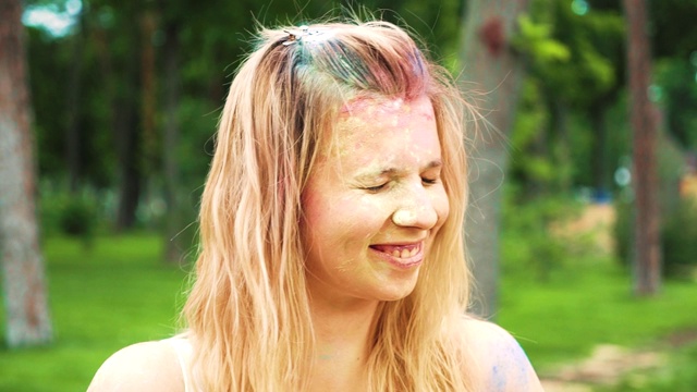 一幅年轻女子的肖像，金发上抹着彩色的粉，对着镜头微笑视频素材