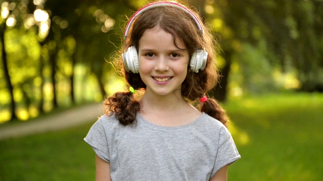 有吸引力的白人小学生女孩的肖像与美丽的棕色眼睛与耳机。快乐微笑的孩子看着相机视频下载