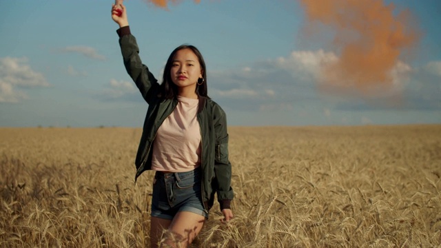 一个亚洲女孩在田野里制造了一团五彩的烟雾视频素材