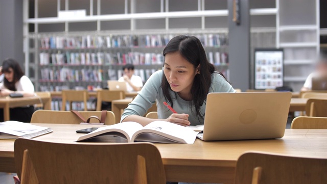 亚洲年轻女学生在图书馆看书和做笔记视频下载