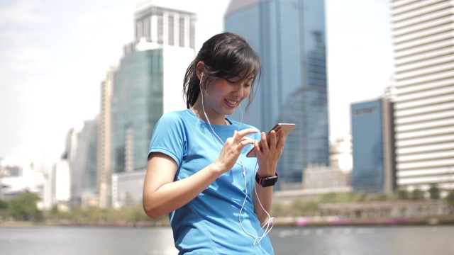 年轻的运动女性在城市里用智能手机听音乐视频素材